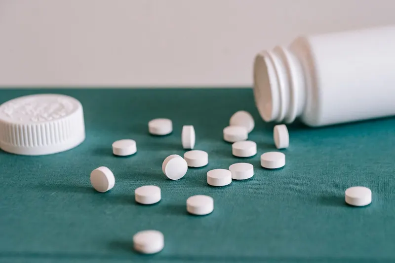 White tablets spilled from an open bottle across a green surface