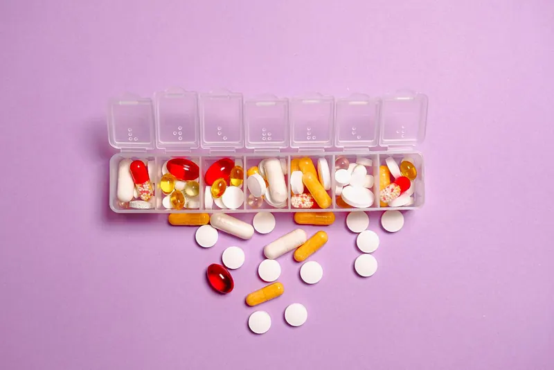 Clear daily pill organizer filled with capsules and tablets on a lilac background
