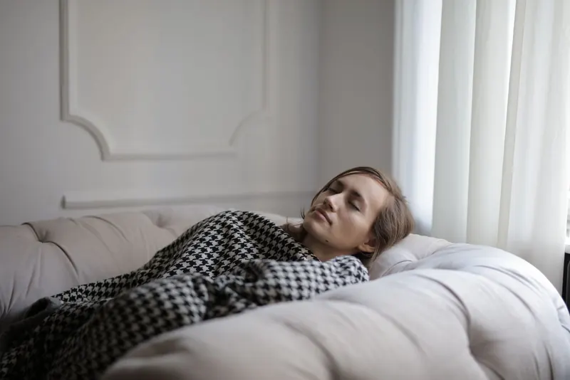 Tired woman resting under a blanket on a couch in a softly lit room
