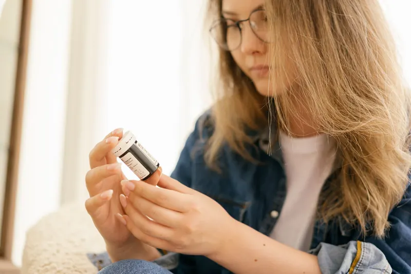 Woman in glasses carefully reading the label on a small supplement bottle